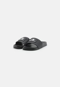 Sandales noires à glissière avec une large sangle portant un logo blanc. Fabriquées en matériau synthétique lisse, avec une semelle plate et un design minimaliste.