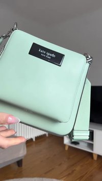 Geantă din piele verde mentă, de tip crossbody, cu o formă rectangulară. Dispune de un plăcuță logo neagră și accente din metal argintiu. Include o curea ajustabilă.