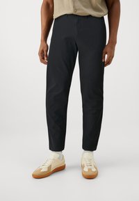 Svarta byxor med rak passform och minimalistisk design, tillsammans med beige sneakers med mockadetaljer och en strukturerad sula.