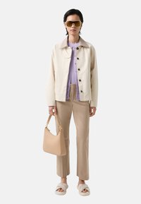 Beige cotton jacket, lavender top, beige trousers, light beige handbag with gold hardware, white sandals with logo detail. Large yellow sunglasses.