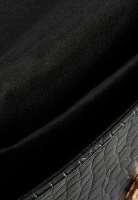 Borsa a tracolla in pelle intrecciata nera con una finitura texturizzata, caratterizzata da un rivestimento interno liscio. Dettagli in hardware dorato e cuciture ben visibili.