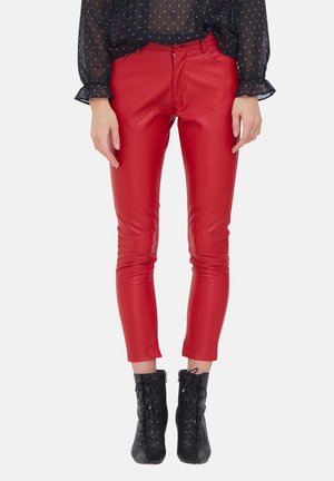 Vrouw die rode leren strakke broek draagt, zwarte veterlaarzen tot aan de enkel en een doorschijnende zwarte blouse met sterrenpatronen.