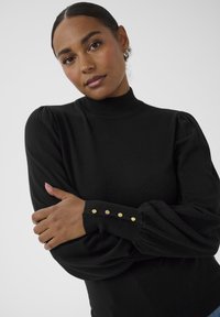 Pulover negru din tricot cu gât înalt, mâneci bufante și nasturi ornamentali aurii pe mansete. Textură netedă și design ajustat.