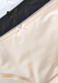 Trois culottes en tissu lisse blanc, noir et beige, chacune avec un petit nœud décoratif et une bordure en dentelle à la taille.