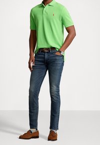 Grön pikétröja med korta ärmar, blå jeans och bruna loafers. Inkluderar en klocka och ett bälte. Hela outfiten är avslappnad med en slim fit.