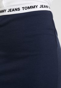 Námořnické strečové džíny s bílým elastickým pasem označeným "TOMMY JEANS." Hladký povrch tkaniny, přiléhavý tvar, s postranními švy.