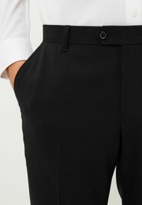Schwarze maßgeschneiderte Hose mit glatter Textur, Knopfverschluss und Seitentasche. Das Material wirkt leicht und strukturiert.