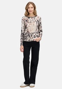 Langermige top met luipaardprint en een textuur grafisch ontwerp met het woord "SPARKLE", gecombineerd met zwarte broek en witte sneakers.