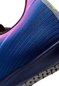 Gros plan d'une chaussure de sport bleue avec des accents roses, une tige en tissu texturé, une semelle épaisse et une semelle extérieure noire cloutée pour une meilleure adhérence.