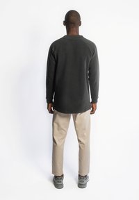 Zwarte longsleeve shirt met een ronde hals, raglanmouwen, gecombineerd met beige broek en grijze sneakers. Eenvoudig en aansluitend ontwerp.