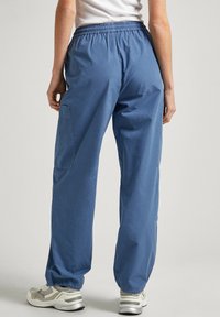 Pantaloni in cotone blu con vita elastica, vestibilità ampia, tasche laterali e orli a costina, abbinati a sneakers sportive grigie.