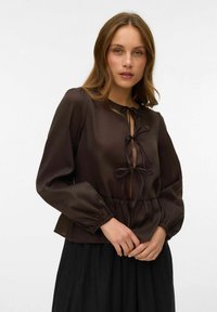 Smeđa bluzica s dugim puf rukavima, teksturirani materijal, v-izrez s detaljem vezanja, nabran struk, uparen s crnom suknjom.