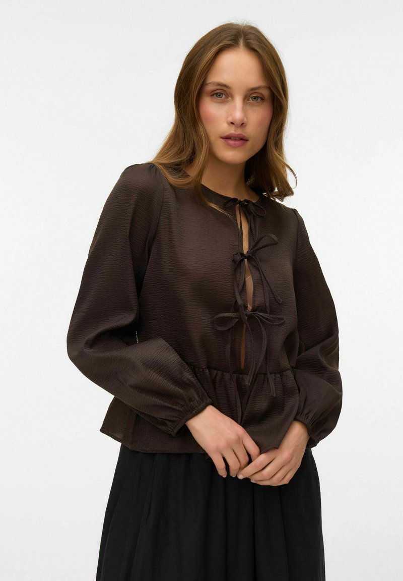 Smeđa bluzica s dugim puf rukavima, teksturirani materijal, v-izrez s detaljem vezanja, nabran struk, uparen s crnom suknjom.