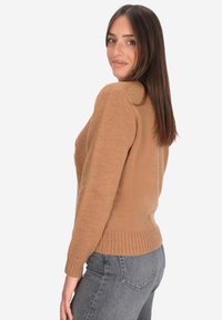 Maglione in bronzo a maglia con orlo e polsini a coste, caratterizzato da una vestibilità comoda e dettagli a punto texturizzato. Abbinato a jeans grigi.