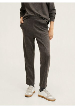 Personne portant un pantalon décontracté gris foncé, un haut assorti à manches longues, des chaussettes noires et des baskets blanches avec des semelles beiges et des bandes velcro.