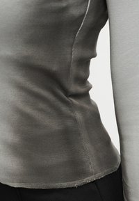 Γκρι εφαρμοστό τοπ με μακριά μανίκια από ριμπ ύφασμα, με εμφανείς ραφές και ελαφρώς καμπυλωτό τελείωμα. Ελαστική υφή με ομαλή επιφάνεια.