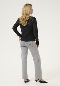 Top in pizzo nero a maniche lunghe con motivi intricati, abbinato a jeans dritti grigi chiari con tasche posteriori e dettagli di cucitura.