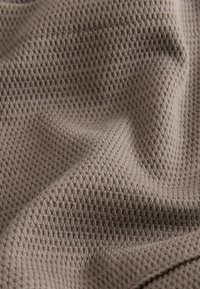 Gros plan sur un tissu marron clair texturé avec un motif en maille gaufrée et des plis doux montrant la profondeur et les détails du matériau.