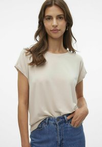 T-shirt beige a maniche corte con scollatura rotonda e una leggera trama, abbinato a jeans blu a vita alta.