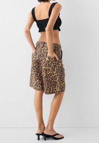 Černý zkrácený top, kraťasy s leopardím potiskem a kapsami, barevná paleta v odstínech béžové a hnědé, hladká textura a černé otevřené pantofle.