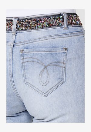 Heledad sinine denim püksid, millel on dekoratiivne helme vöökoht. Tagakoti disain sisaldab peent keeriseid tikandit.