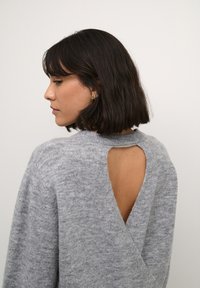Grå strikket sweater med en unik udsnit på ryggen, blød tekstur og klassisk rund halsudskæring. Stoffet er let og afslappet.