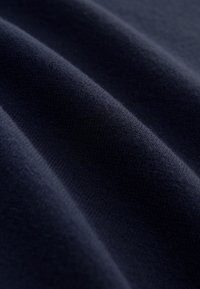 Tumši zila auduma ar gludu, mīkstu tekstūru, kas raksturojas ar smalku elastību un viļņveida rakstu, kas liecina par adītu materiālu.