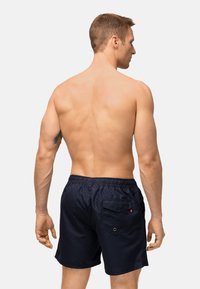 Pantaloni da bagno navy con cintura elastica, cordoncino e dettagli sulla tasca posteriore. Tessuto liscio e leggero, ideale per l'abbigliamento da spiaggia.