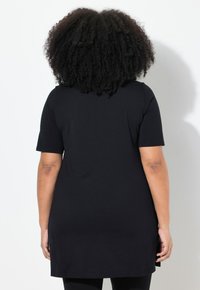 Černá tuniková halenka s krátkým rukávem, rovného střihu a postranními rozparky, vyrobená z měkké tkaniny. Zadní strana má hladký, nezdobený povrch.