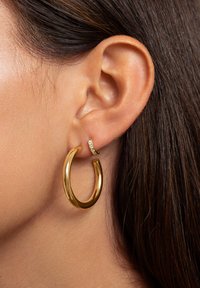 Goldene Creolenohrringe mit glänzender Oberfläche und glatter Textur, kombiniert mit einem kleinen, funkelnden Stecker, der klare Steine enthält.