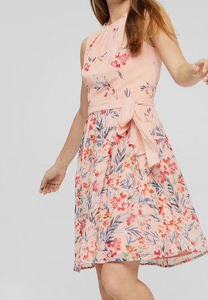 Robe légère sans manches rose pâle avec un imprimé floral, un col plissé, une ceinture à la taille et une jupe fluide portée par une femme en mouvement.