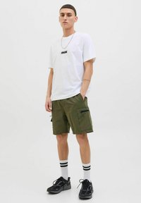 Un tricou alb cu logo negru, pantaloni scurți cargo verde măsliniu cu buzunare laterale, adidași negri și șosete albe cu dungi negre.