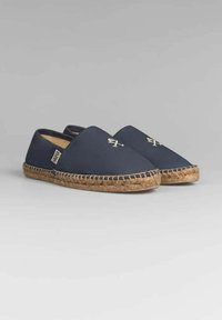 Espadrilles de lona azul marino con suela trenzada de yute, que presentan un diseño de emblema sutil en la parte superior y un estilo sin cordones para facilitar su uso.
