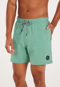 Pantaloncini da bagno verde menta realizzati in tessuto testurizzato. Presentano un elastico in vita con un cordino in bianco e nero e una patch con il logo sul lato.