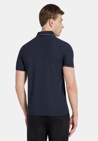 Granatowa koszulka polo z gładkiego materiału, z klasycznym kołnierzykiem, krótkimi rękawami i kontrastowym przeszyciem przy mankietach.