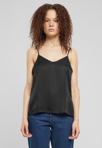 Top in satin nero con spalline sottili, design a V, texture liscia e vestibilità rilassata, abbinato a jeans in denim blu.