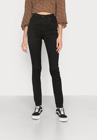 Jeans skinny pretos de cintura alta com uma textura suave, combinados com ténis em preto e branco com um design de atacadores e sola plataforma.