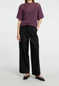 Woman wearing a purple short-sleeve knit sweater, black wide-leg trousers, black pointed-toe slingback flats, standing with one hand in pocket.