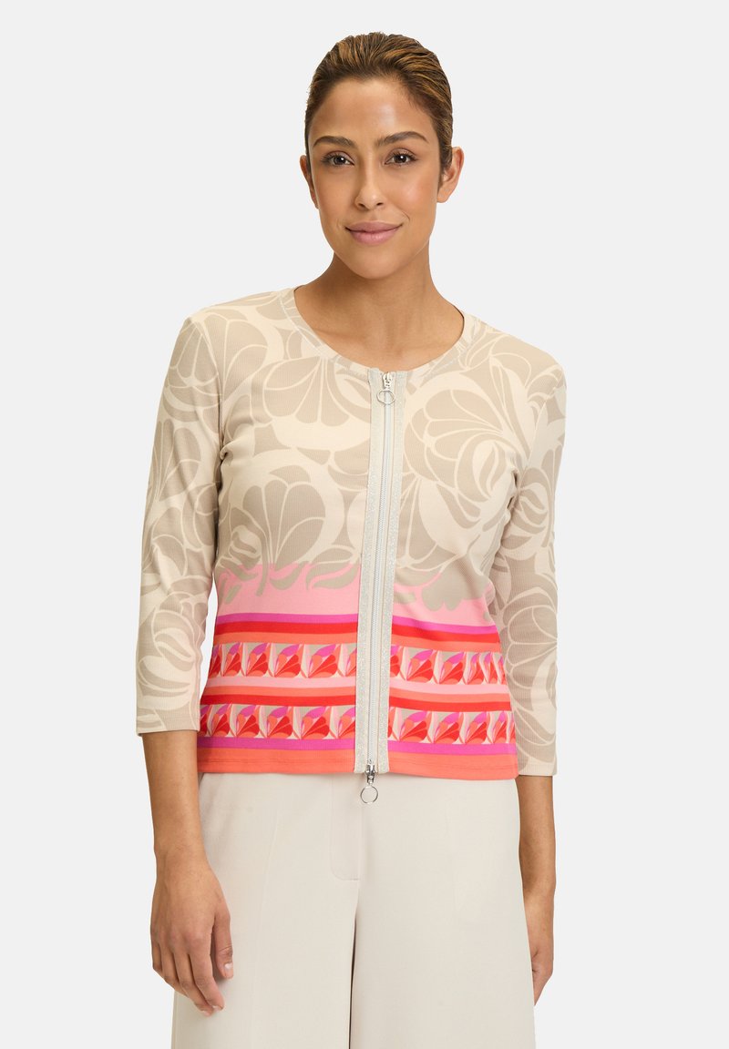 Cardigan zippé avec un motif floral dans des tons beige et rose, présentant des manches trois-quarts et des accents géométriques au niveau de l'ourlet.