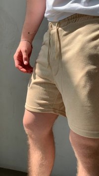 Beige puuvillashortsit, joissa on elastinen vyötärö ja nauha, sivutaskut ja pehmeä, teksturoitu pinta.
