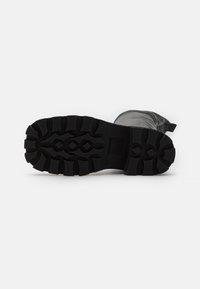 Suela de bota de goma negra con ranuras profundas y dibujos para agarre; diseño resistente con patrón elevado y superficie texturizada.