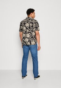 Schwarz Kurzarmhemd mit cremefarbenem floralen Muster, kombiniert mit blauen Denim-Jeans und schwarzen Schuhen. Glattes Material und lockere Passform.