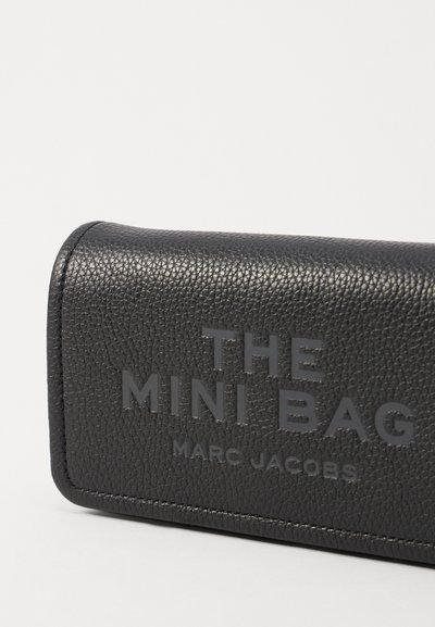 Czarna torba ze skórzanym wykończeniem z wytłoczonym napisem "THE MINI BAG" oraz "MARC JACOBS". Prostokątny kształt z zaokrąglonymi krawędziami.
