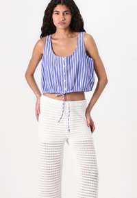 Top corto a righe blu e bianche con scollatura tonda e chiusura con bottoni, abbinato a pantaloni ampi bianchi in maglia texturizzata.