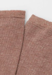 Gros plan sur un tissu tricoté à rayures de couleur rose-brun avec un détail de bord replié sur deux bords de vêtement qui se chevauchent.