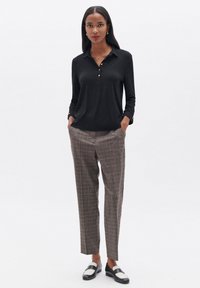 Camicia nera a maniche lunghe con colletto abbottonato, abbinata a pantaloni su misura a quadri marroni. Calzature con mocassini bianco e nero.