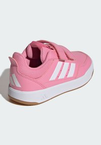 Różowy but sportowy z gładką, syntetyczną cholewką, białymi paskami, szczegółami z siateczki oraz gumową podeszwą. Wyposażony w pasek na rzep.