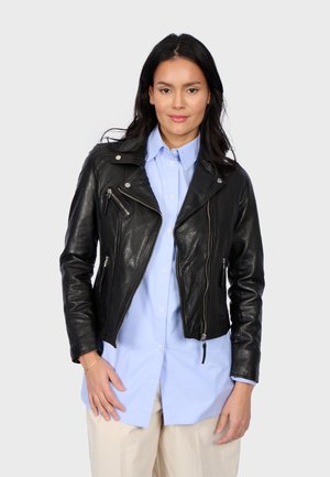 Veste de motard en cuir noir avec quincaillerie argentée, présentant des zips asymétriques et une coupe ajustée, portée sur une chemise bleu clair.