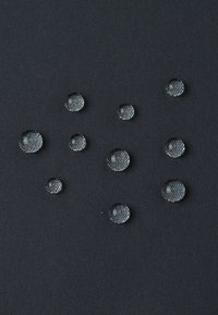 Czarna tkanina z wieloma przezroczystymi kroplami wody o różnych rozmiarach, spoczywającymi na gładkiej, teksturowanej powierzchni. Brak wyraźnych wzorów lub elementów metalowych.