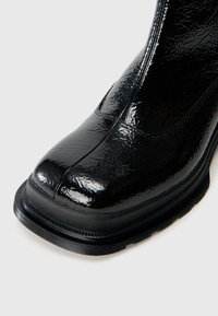 Czarne, lakierowane ankle boots z błyszczącym, teksturowanym wykończeniem, kwadratowym noskiem i grubą, czarną gumową podeszwą. Subtelne detale w postaci przeszyć wzdłuż boków.